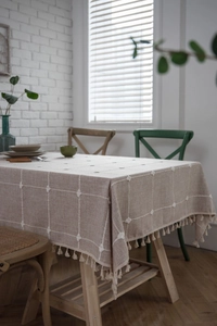 Close-up of beige cotton linen tablecloth with grid embroidery and fringe tassel edges