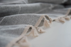 Detail of grey checkered linen tablecloth featuring elegant white fringe tassels