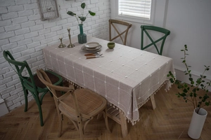 Detail of beige linen tablecloth featuring white grid patterns and elegant fringe trim