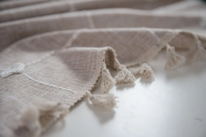 Close-up of beige woven tablecloth featuring white geometric lines and elegant tassel fringe