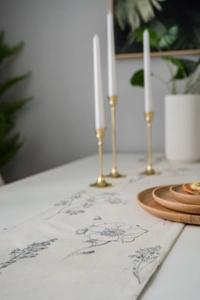 Close-up of sketch floral table runner with tassels on a white wooden table surface