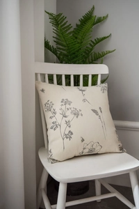 Close-up of linen pillow with grey floral and bee prints on a white wooden chair