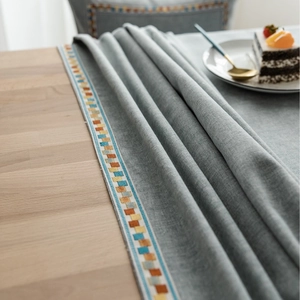 Gray linen tablecloth with geometric embroidery and modern tassel accents on wood table