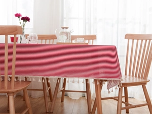 Close-up of red and white striped tablecloth with cream tassels on a wooden table