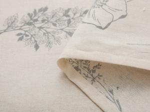 Close-up detail of beige linen fabric texture with grey floral print and stitched edge