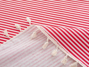 Detail of red and white striped tablecloth with cream cotton tassels and hemmed edges