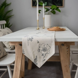 Floral table runner with bee embroidery and tassels on a white wooden table