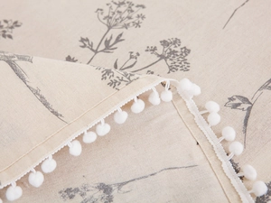 Detail of floral linen fabric cover with decorative white pom-pom fringe trim