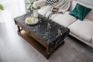 Detail of black marble pattern tablecloth with white pom-pom fringe on a wooden table