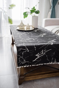 Detail of black marble pattern table runner with white pom-pom fringe on wooden desk