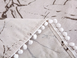 Detail of marble pattern fabric cover with white pom-pom fringe and woven texture