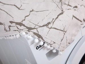 Detail of white marble print dust cover with elegant pom pom tassels on a washing machine