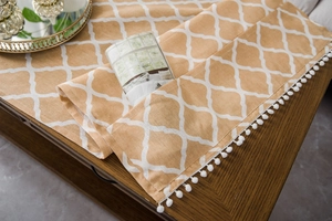 Detail of yellow cotton linen table runner with white geometric pattern and pom pom fringe