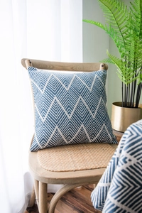 Detail view of navy blue and beige geometric knit pillow on a wooden chair with plants