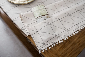 Detailed close-up of beige cotton linen table runner with black geometric lines and white pom-poms