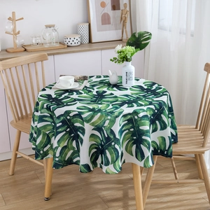 Detailed view of waterproof round tablecloth with green monstera leaf print on a wood table