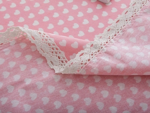 Close-up of pink linen tablecloth with white heart patterns and delicate lace edge