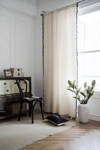 Detail of cream linen curtain with black pom-pom fringe and metal hook hanging style