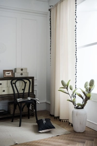 Detail view of off-white linen curtains with black tassel trim in a modern room