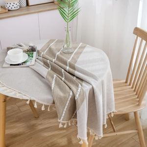 Round linen tablecloth with beige and brown stripes and white tassel trim on a table