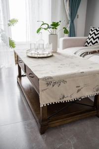 Close-up of linen table runner with floral print and white tassel trim on wood table