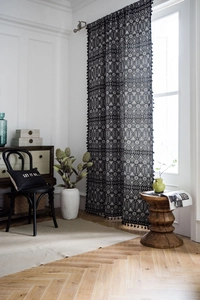Detail of bohemian geometric curtains with black tassel trim and semi-sheer fabric texture