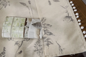 Detail of linen table runner with floral print, pom-pom trim and a functional side pocket