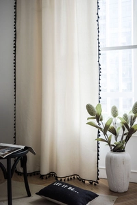 Detail of minimalist cream curtain fabric with decorative black tassel trim for windows
