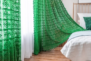 Close-up of green crochet curtain with geometric floral patterns and fringe details