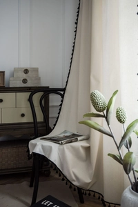 Detail view of cream cotton linen curtain featuring elegant black tassel fringe trim