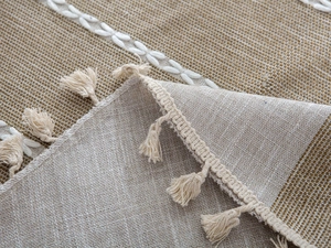 Detail of linen table runner featuring beige fringe tassels and white embroidered patterns
