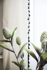 Detail view of realistic faux greenery branch with decorative black tassel on white curtain