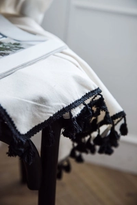 Detail of off-white minimalist curtain with black tassel fringe on a wooden chair