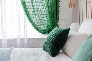 Close-up of green crochet lace curtain with floral patterns and pompom tassels