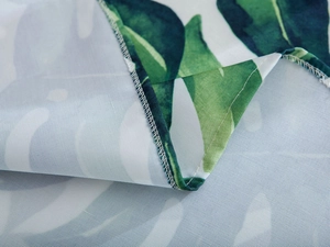 Close-up of waterproof green monstera leaf tablecloth with detailed white double-stitched edges