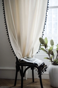 Detail of cream linen curtain with black tassel fringe and elegant drape texture
