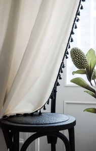 Detail of cream linen curtain with black tassel fringe draped on a black stool