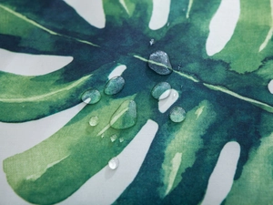 Close-up of waterproof fabric featuring green monstera leaf print with clear water droplets