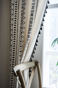 Close-up of bohemian linen curtain with black geometric prints and black tassel edges