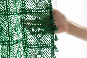 Detail of dark green crochet lace curtain with floral patterns and delicate tassels