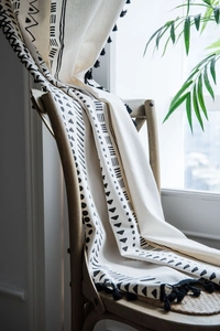 Detail of bohemian cotton linen fabric with black geometric prints and pompom fringe