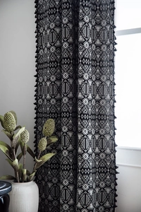 Close-up of bohemian geometric patterns and black pom-pom tassel fringe on cotton curtain