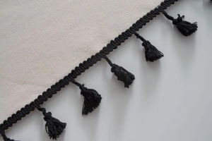Close-up of cotton linen fabric featuring black wavy trim and delicate handmade tassels