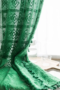 Detail of forest green crochet lace curtain with geometric hollow patterns and tassels