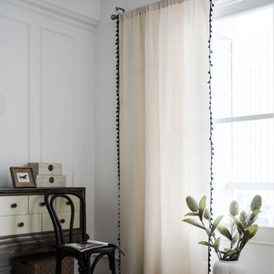 Minimalist beige cotton linen curtain with black pompom tassels in a vintage room setting