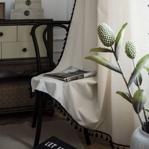 Minimalist white semi-sheer curtain with black tassels draped over a vintage chair