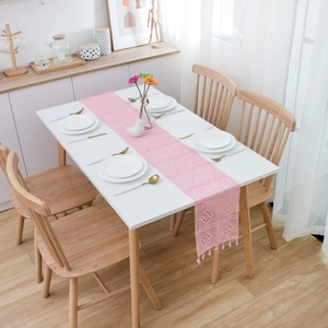 Pink hand-crocheted hollow table runner with fringe tassel on a white dining table