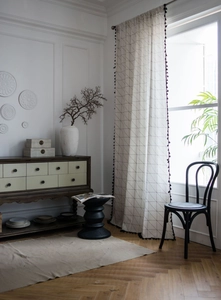 Close-up of geometric white linen curtain with black tassels and mesh print pattern