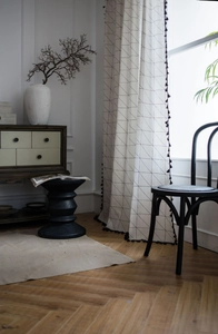 Detail of off-white curtain featuring black geometric patterns and delicate tassel edges