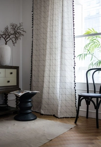 Detail of white cotton linen curtain with black geometric grid and tassel fringe trim